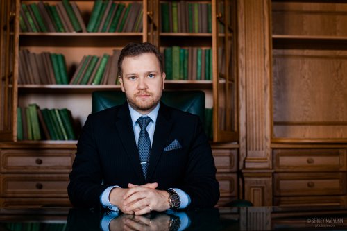 Деловой мужской портрет предпринимателя в костюме за столом в кабинете с книжным шкафом для бизнес съемки