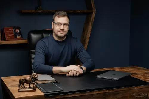 Деловой портрет мужчины в очках за рабочим столом в современном кабинете для корпоративной съемки