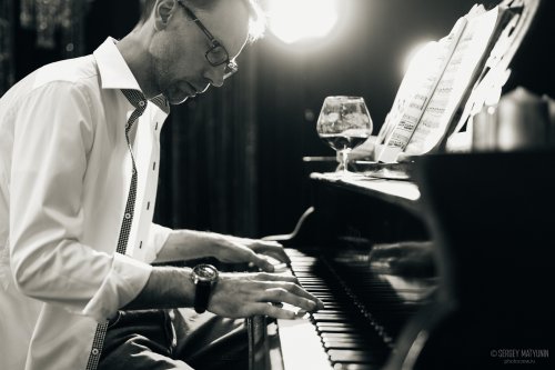 Мужчина в белой рубашке играет на рояле во время репортажной съемки выступления в ресторане