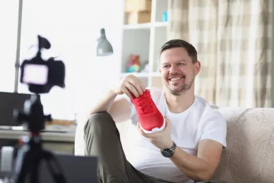 Smiling man demonstrates sneaker on video camera. Introducing new product blog concept